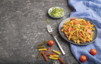 Tortiglioni semolina pasta with tomato and microgreen sprouts on a black concrete background and