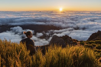 Woman sitting on a mountain watching the sunset over a sea of clouds, Pico Ruivo, Madeira,