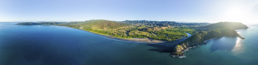 Panoramic aerial view of a green forested coastal landscape with blue sea and sky, Pochote,