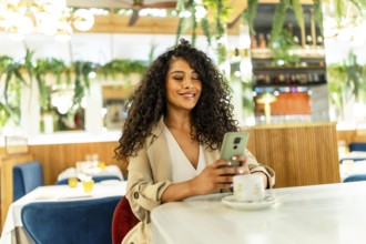 Beauty latin woman using mobile phone sitting on a cafeteria drinking coffee alone