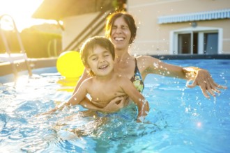 Mother and son are playing and laughing together in a home swimming pool during a sunny summer
