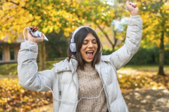 Happy vital caucasian young woman dancing listening to music in a park with fallen leaves in a