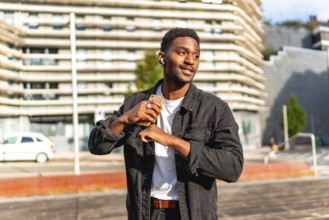 African man listening to music using small wireless earbuds and dancing in the city