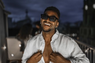 Latin brunette sensual man in sunglasses dancing during night party in a rooftop with multi-ethnic