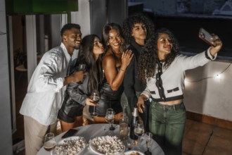 Happy multiracial friends grimacing while taking selfie with cellphone during night roof party
