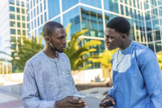 Two senegalese businessmen wearing traditional dashiki attire are discussing business while holding