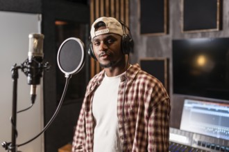 Young african american artist wearing headphones and baseball cap, recording a new album in