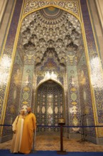 Omani couple in traditional dress in front of the golden prayer niche in the Sultan Qabus Grand