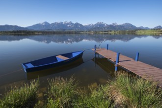 A jetty with a blue boat on a quiet lake with an impressive mountain view, Hopfen am See, near
