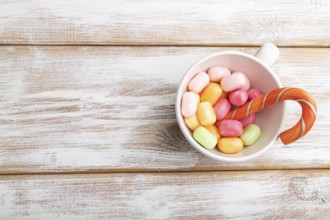 Heap of multicolored caramel candies in cup on white wooden background. copy space, top view, flat