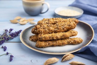 Crumble cookies with seasme and almonds on ceramic plate with cup of coffee and blue linen textile