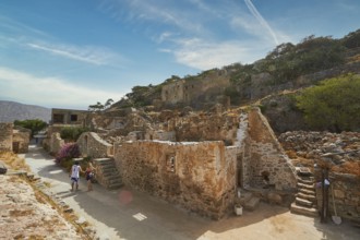 Tourists walking through an ancient village with ruins and pathways on a sunny day, Venetian Sea
