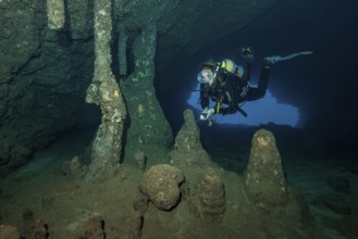 Scuba diver female diver swimming dives in entrance area of underwater cave stalactite cave