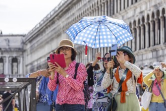 Tourists from Asia with mobile phones and parasols taking photos. Souvenir photo of St Mark's