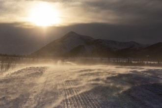 Snow-covered gravel road in the wind in front of mountains, backlight, ice, Dalton Highway, Alaska,
