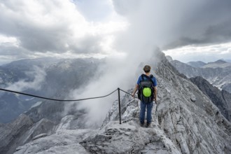 Mountaineer on a narrow rocky ridge on a steel cable, Watzmann crossing to Watzmann Mittelspitze,