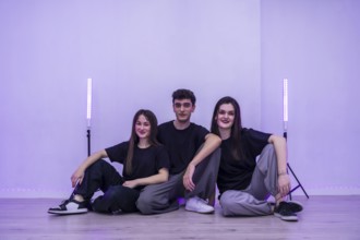 Three young dancers are sitting together on the floor of their dance studio, taking a break and