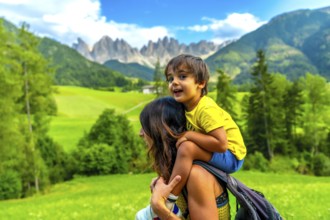 Mother carrying her son on her shoulders while enjoying the view of the odle mountains and the