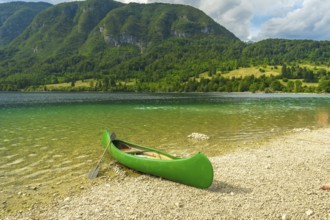 Green canoe sits on the pebbled shore of lake bohinj, inviting visitors to explore the stunning