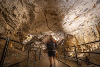 Tourist walking on a concrete walkway inside the famous postojna cave in slovenia, admiring the