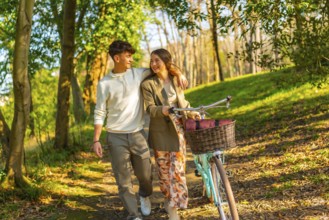 Happy young couple walking through a sunlit forest path with a vintage bicycle, embracing the