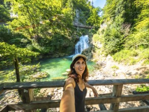 Woman taking selfie with waterfall and turquoise colored water of tolmin gorges in the background,