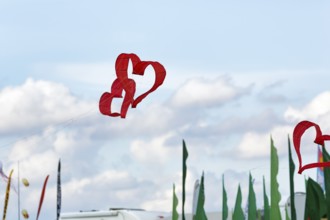 Two red heart-shaped kites flying intertwined in the sky, text free space, kite festival in