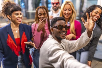 Multi-ethnic friends waving at camera taking selfie during a night party in a bar terrace