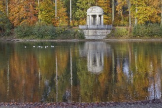 An ancient temple is reflected in an autumnal pond with vibrant colours, Stadtwald, Krefeld