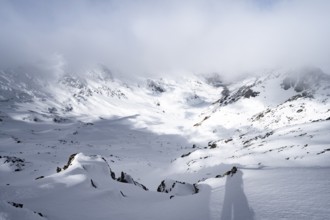 View of cloudy valley from the summit of Piz Laviner, mountain landscape in winter, Grisons Haute