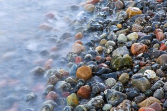 Blurred sea water of wave rolling over wet colourful pebbles on shingle beach, cobble beach