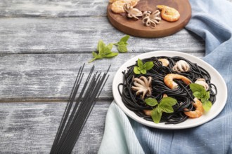 Black cuttlefish ink pasta with shrimps or prawns and small octopuses on gray wooden background and