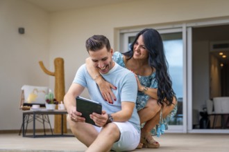 Woman embracing her boyfriend while using tablet sitting in the patio of a new house