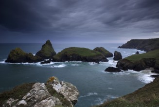 Dramatic clouds on rocky coast, rising rain shower over rocky islands with foaming surf, Kynance