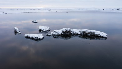 Snow-covered small islands overgrown with bushes in Lake Myvatn, at blue hour, Kalfaströnd, drone