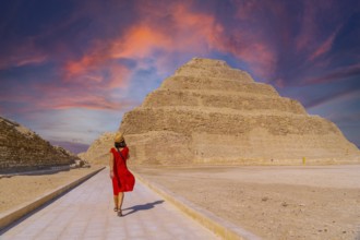 A young tourist in a red dress at the Stepped Pyramid of Djoser at sunset, Saqqara. Egypt. The most