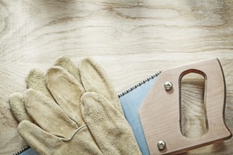 Pair of leather protective gloves sharp hacksaw on wooden board construction concept