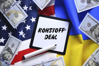 The flags of Ukraine and USA with dollar notes and plaque with the inscription raw materials deal,