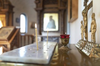 Candles burn in front of the iconostasis and the cross with a crucifix in a small Orthodox chapel