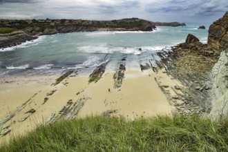 Giant rough gray rocks and smooth sandy beach. Noon on the beach of Playa di Arnia, Spain. Rocky