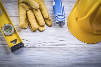 Assortment of working gloves hard hat blue rolled blueprints construction level on wooden board