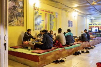 A group of people sit on traditional platforms and enjoy a meal together in a restaurant,