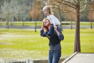 Mother holding daughter sit in her shoulders at the park lake