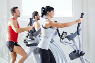 Man and woman with elliptical cross trainer in sport fitness gym club