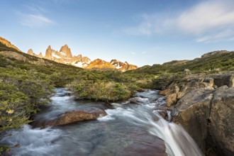 A waterfall with the Fitz Roy mountain illuminated by the morning sun in the Los Glaciares National