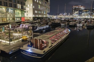 Illuminated boat in a harbour at night surrounded by modern buildings and reflections in the water,