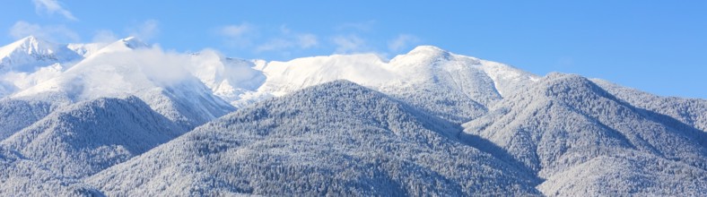 Winter travel vacation nature panoramic background with snow covered mountain peaks and blue sky
