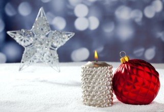 Christmas card of silver star bauble and candle on snow and blue background