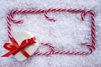 Christmas gift and candy cane frame on snow background