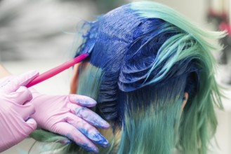 Side view of process of dyeing hair in unique color. Hairdresser in protective glove using pink